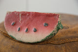 Visible wear, chipped paint, and wire loop detail on the vintage clay watermelon bank.
