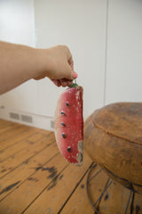 Hand holds vintage clay watermelon piggy bank showing red paint and edge wear.