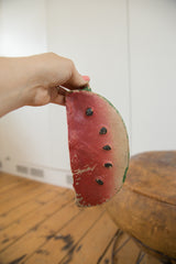 Hand holding chipped, aged top edge of clay watermelon bank with red and green.