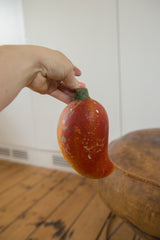 Hand holding vintage folk art chili pepper piggy bank, showing aged reddish-orange paint and chips.