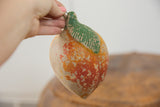 Hand holding the vintage folk art clay mango's green leaf and distressed, chipped surface.