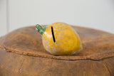 Vintage Mexican folk art mango bank showing coin slot and chipped yellow finish.
