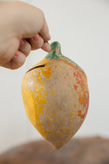 Bottom of vintage clay mango, showing chipped yellow and reddish-orange paint, aged texture.