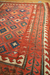 Close-up of the antique Caucasian rug's geometric diamond patterns and reciprocating wave border.