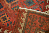 Folded antique Caucasian rug reveals geometric pattern, exposed foundation, light tatter, and machine binding.