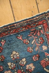Vintage Lilihan sampler rug corner: indigo field, blush floral motifs, red border, tattered edge.