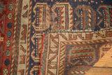 Antique Kurdish square rug folded, revealing worn indigo, red geometric pile, exposed foundation.