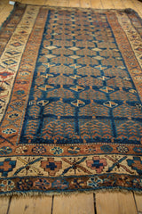 Vintage Kurdish rug's geometric border and worn navy main field with shrub motifs.