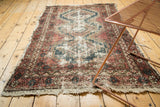 Worn texture and tattered edges of a vintage Hamadan rug, revealing faded red and blue.