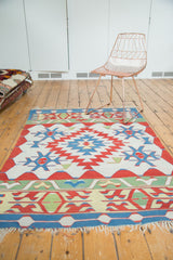 Fringed end detail of a Vintage Turkish Kilim rug showing banded red, sky blue, and saffron patterns.