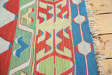Turkish Kilim rug edge detail: sky blue border, ivory floral design, and natural fringes.