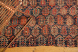 Worn indigo blue and madder red boteh motifs on an antique Afshar rug fragment's raw edge.