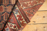 Folded antique Afshar rug fragment with madder red, indigo boteh motifs, and worn edges.