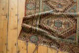 Hamadan rug detail with geometric diamond contour, hook motifs, and wave border in apricot, blue, brown.