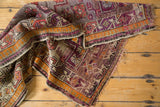Antique Caucasian rug's geometric vinery in aubergine and tangerine with tattered edges.
