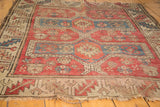 Angled vintage Caucasian rug, dusty rose, blue geometric medallions, worn fringe.