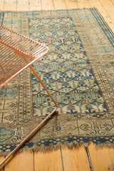 Worn geometric stylized buds in blues and beige on an antique Caucasian rug with tattered end.