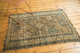 Antique Caucasian rug corner, displaying geometric blue, charcoal, and ivory motifs, with tattered edge.
