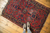Corner of vintage Dargezine rug, red field, indigo herati pattern, meandering vines, tattered fringe.