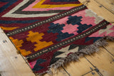 Close-up of vintage Kilim runner with pink, wine, tangerine geometric motifs and worn edge.