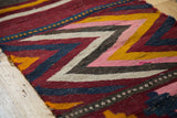 Textured close-up of vintage hand-woven Kilim featuring colorful chevron and pearl design.
