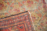 Worn saffron and red Zuli Sultan rug corner revealing hand-knotted foundation and tattered fringe.