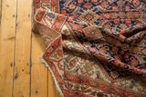 Folded vintage Malayer runner showing Herati motif in red, navy, and beige with a vine border.