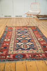 Kurdish rug fragment corner showcasing indigo, red, and beige stylized arabesque border and fringe.