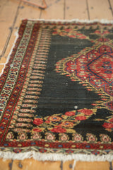 Angled close-up of an Antique Senneh rug showing intricate red floral patterns, boteh motif, and worn fringe.