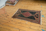 Antique Persian Senneh rug with tattered end fringe, dark field, and detailed red floral border.