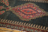 Antique Senneh rug detail: intricate red medallion, worn charcoal field, boteh border, and tattered end.