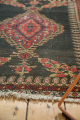 Antique Senneh rug detail: charcoal field, intricate red budding flowers, boteh border, tattered fringe.