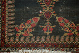 Intricate madder red and gold floral motifs, boteh border, and worn fringe on an antique Senneh rug corner.