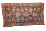 Antique Soumac rug with navy blue field, elongated gold medallions, and cherry red geometric motifs.