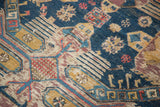 Antique Soumac rug close-up: navy, gold, red geometric finned motifs, visible etching.