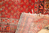 Folded corner of antique Malayer rug, showing hand-knotted foundation and tattered ivory fringe.