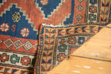 Vintage Caucasian rug corner shows madder red, indigo blue geometric patterns, tattered ends, reverse.