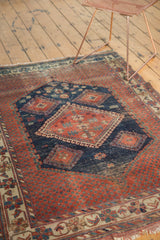 Antique Afshar rug with worn red field, navy diamond medallion, visible foundation, tattered fringe.