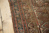 Tattered edge of antique Persian Kamseh rug, revealing worn pile, geometric motifs, exposed foundation.