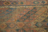 Antique Kurdish carpet: geometric motifs in dusty copper, blue, gold, showing exposed foundation and tatter.