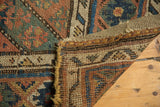 Antique Kurdish carpet's hand-knotted foundation, tattered side, and worn geometric pattern.