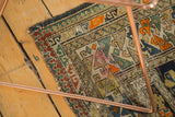 Worn corner of antique Caucasian rug, displaying geometric motifs in tangerine, mallard green, and sand hues.