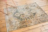Distressed Hamadan rug corner, revealing geometric pattern and worn foundation in sand and seafoam.