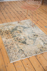 Distressed Hamadan rug corner, with faded geometric pattern, sand, seafoam green, and secured fringe.