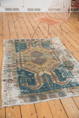 Corner of a distressed vintage Hamadan rug, showing worn knot heads, faded teal, and gold.