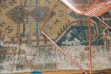 Distressed vintage Hamadan rug displaying faded teal, gold geometric patterns and textured wear.