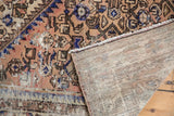 Distressed Hamadan rug's hand-knotted foundation revealed, showing pile wear and primitive motif.