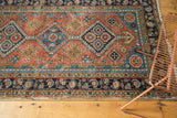 Hand-knotted Persian Heriz rug's navy border with floral details, terracotta field, and aged pile.