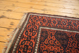 Antique Persian Belouch rug corner detail: madder red, navy geometric gul motif, intact selvage.