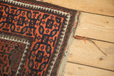 Antique Belouch rug corner showing madder red, navy geometric gul motifs, ivory, and fringe.